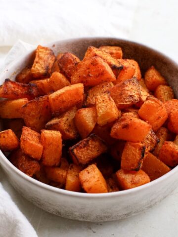 A bowl of orange roasted seasoned butternut squash cubes in a white bowl.