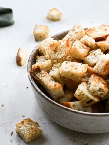 A bowl of homemade vegan croutons with some spilling out of the bowl.